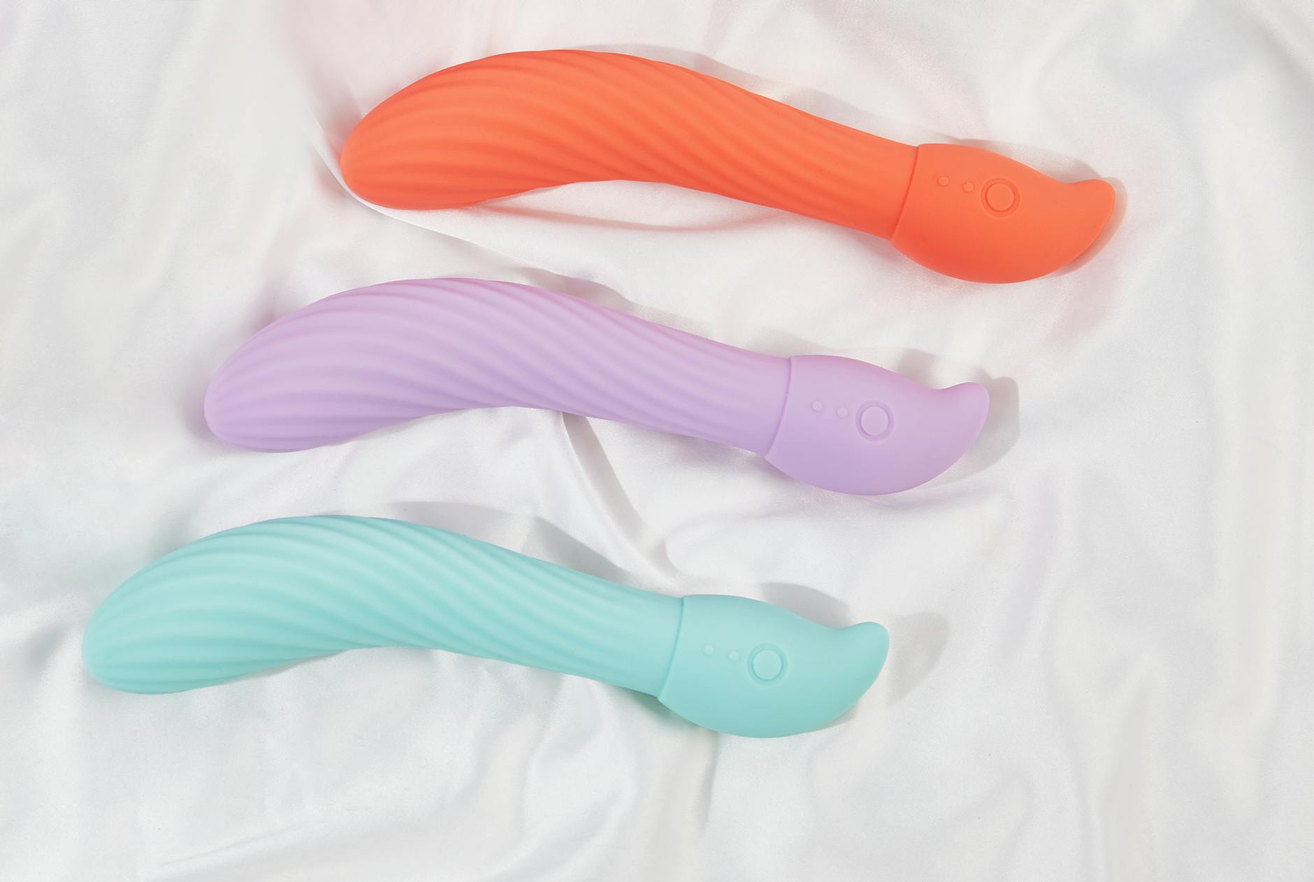 Três vibradores coloridos dispostos em tecido branco, destacando a textura suave de brinquedos de silicone