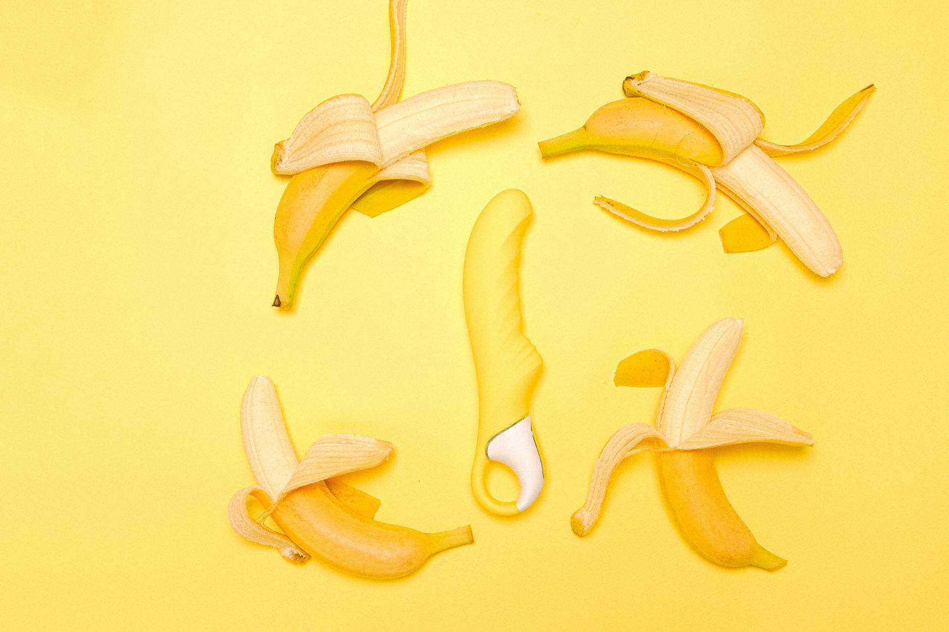 Vibrador de limão amarelo em silicone cercado por bananas descascadas em fundo amarelo