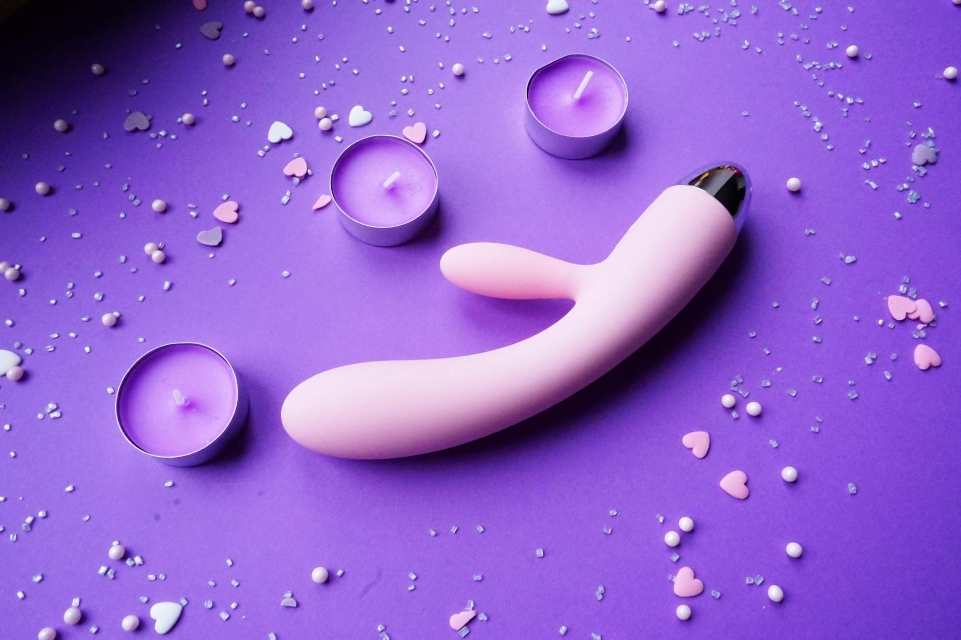 Vibrador rosa em fundo roxo com confete de corações e velas para ambiente romântico