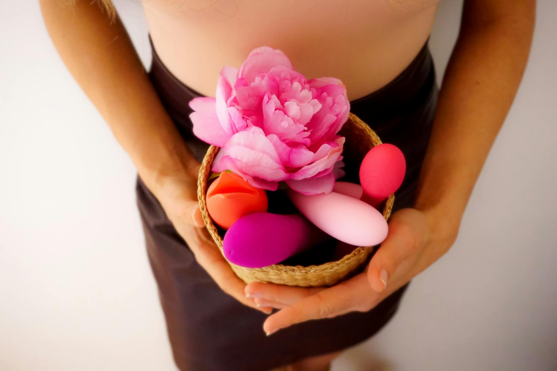 Mulher segurando um vibrador rosa em suas mãos, com livros de arte ao fundo, simbolizando intimidade e autodescoberta pessoal